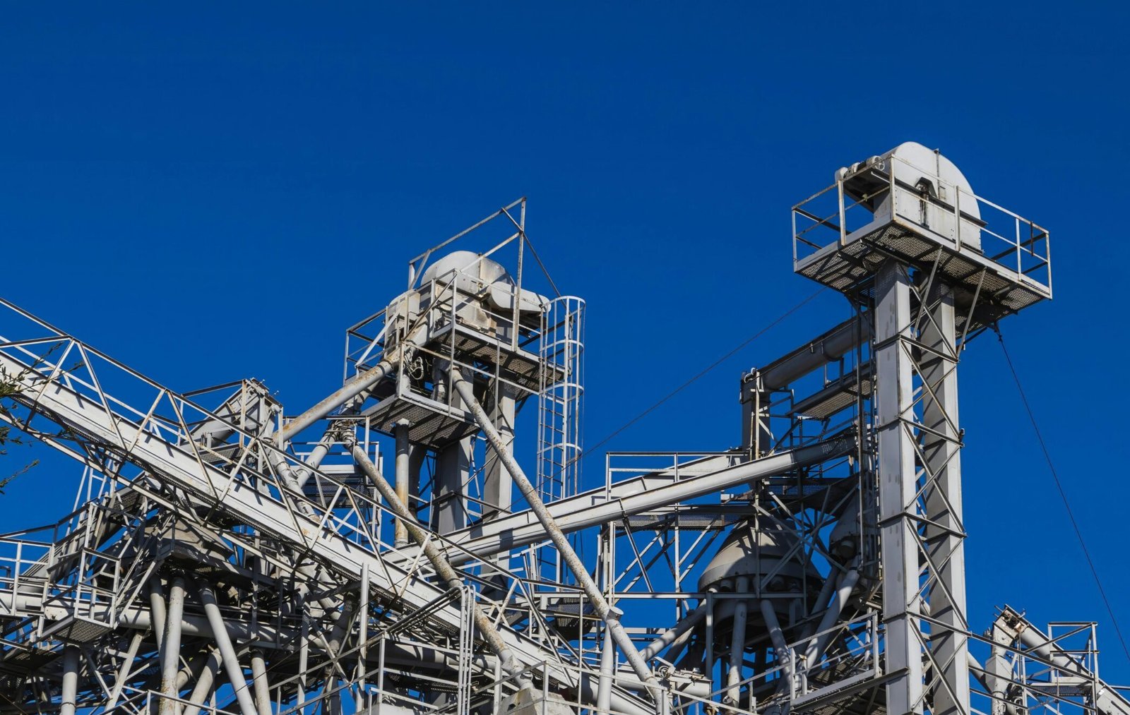 Grain Silo & Handling Equipment Detailed view of metal industrial structures with pipes and beams against a clear blue sky.